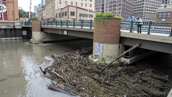 MILWAUKEE, WISCONSIN - AUGUST 10: People watch as debris piles up on a bridge piling on the Milwaukee River after heavy rain in the area on August 10, 2025 in Milwaukee, Wisconsin. Heavy downpours brought as much as 13 inches of rain to parts of southeast Wisconsin overnight, resulting in widespread flooding across the region. (Photo by Andy Manis/Getty Images)