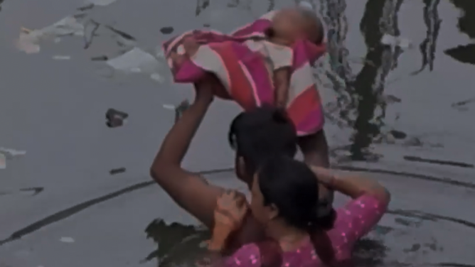A man holds a baby over his head as he wades through heavy flooding in India.