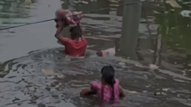 The second man now holds the baby over his head, while the first man and the woman on his back follow behind him.
