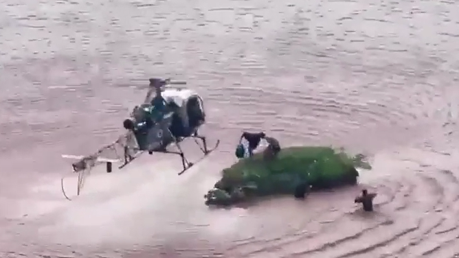 The indian Army helicopter picks up two people needing rescue from a grassy patch above flooding.