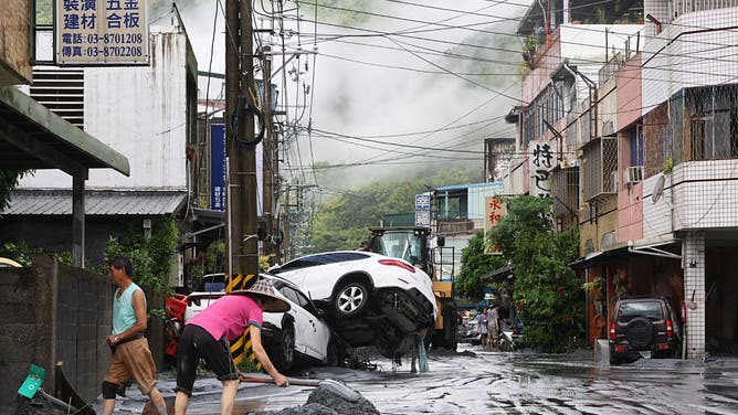 Residents clear mud from their property, while damaged cars are seen in the background, in Hualien on September 24, 2025, following the bursting of a barrier lake. At least 14 people were killed when a decades-old lake barrier burst in Taiwan, a government official said on September 24, after Super Typhoon Ragasa pounded the island with torrential rains.