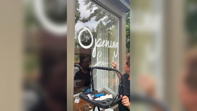 Someone paints an "opening soon" sign on a shop window in Historic Biltmore Village.