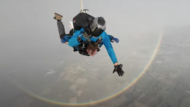 Skydivers dropping to Earth near a rainbow in its true form.