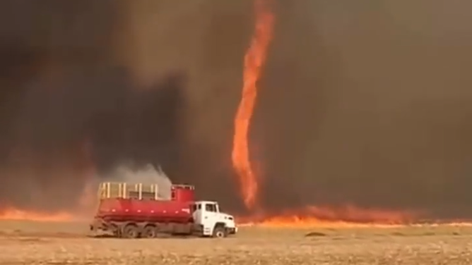 Fire truck sprays water on flames as firenado spins up behind it.