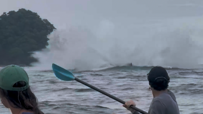 The whale splashes back down into the water, sending waves toward the kayakers.