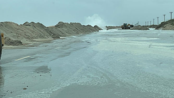 North Carolina Department of Transportation crews work to clear sand from Highway 12 on Hatteras Island, North Carolina on Saturday, Oct. 12, 2025.