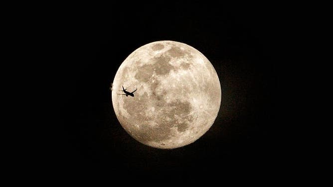 An airplane flies across the Supermoon full moon as it rises over Bekasi Regency, West Java province, Indonesia, on October 6, 2025.