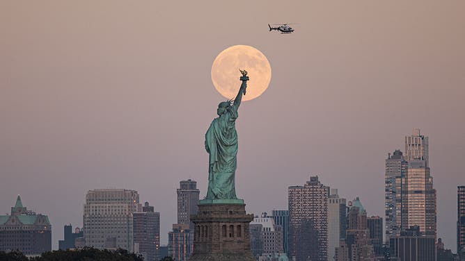 The full Harvest Supermoon rises behind the Statue of Liberty in New York City on October 7, 2025, as seen from Jersey City, New Jersey.