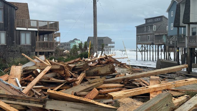 A few homes stand in the background of a pile of debris from collapsed homes in Buxton.