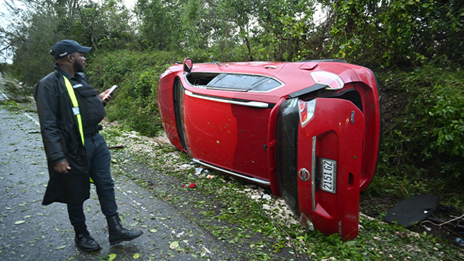A police officer inspects a car damaged by a fallen tree after the passage of Hurricane Melissa in Manchester, Jamaica, on October 28, 2025. Hurricane Melissa ripped up trees and knocked out power after making landfall in Jamaica on October 28, 2025 as one of the most powerful hurricanes on record, inundating the island nation with rains that threaten flash floods and landslides. (Photo by Ricardo Makyn / AFP) (Photo by RICARDO MAKYN/AFP via Getty Images)