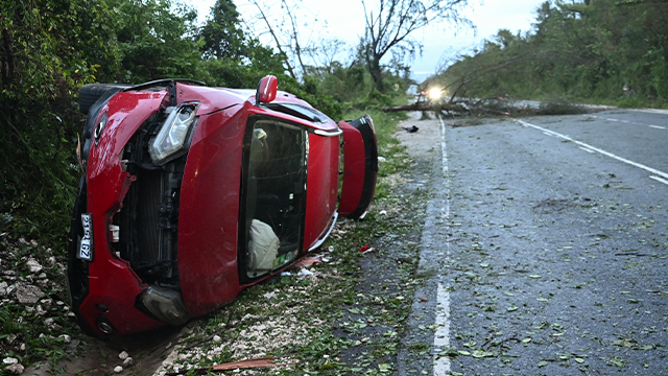 A damaged car by a fallen tree is seen after the passage of Hurricane Melissa in Manchester, Jamaica, on October 28, 2025. Hurricane Melissa ripped up trees and knocked out power after making landfall in Jamaica on October 28, 2025 as one of the most powerful hurricanes on record, inundating the island nation with rains that threaten flash floods and landslides. (Photo by Ricardo Makyn / AFP) (Photo by RICARDO MAKYN/AFP via Getty Images)