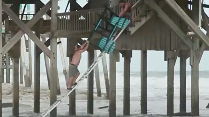 Two men used a ladder to scale a damaged house to salvage belongings after the stairs were destroyed in Buxton, North Carolina.