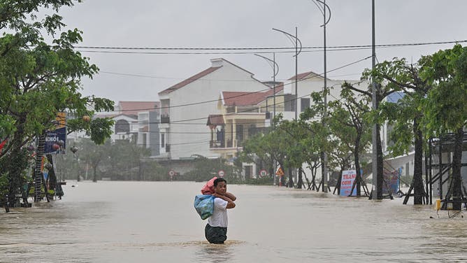 A man carries belongings as he wades through a flooded street during heavy rains in Hoi An on October 30, 2025. Vietnam's coastal provinces have been lashed by heavy rains since October 26, with a record of up to 1.7 metres (five feet seven inches) falling over 24 hours. 