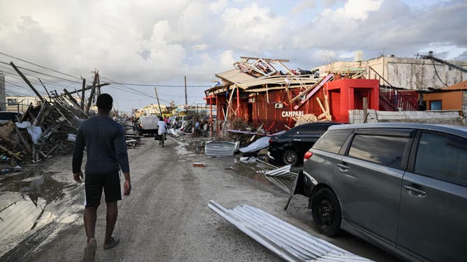 TOPSHOT - A man walks past a car and damaged buildings October 29, 2025 following the passage the previous day of Hurricane Melissa, in Black River, St. Elizabeth, Jamaica. Hurricane Melissa bore down on the Bahamas October 29 after cutting a path of destruction through the Caribbean, leaving 30 people dead or missing in Haiti and parts of Jamaica and Cuba in ruins. Somewhat weakened but still threatening, Melissa will bring damaging winds and flooding rains to the Bahamas Wednesday before moving on to Bermuda late Thursday, according to the US National Hurricane Center (NHC). (Photo by Ricardo Makyn / AFP) (Photo by RICARDO MAKYN/AFP via Getty Images)