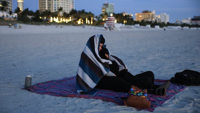 MIAMI BEACH, FLORIDA - NOVEMBER 11: Two people (who did not want to provide their names) bundle up against the chilly air as they watch the sunrise on the beach on November 11, 2025 in Miami Beach, Florida. A cool blast of air moved through the area in the morning with temperatures in the upper-40s all across South Florida, and with wind chill it was in the low- to mid-40s.