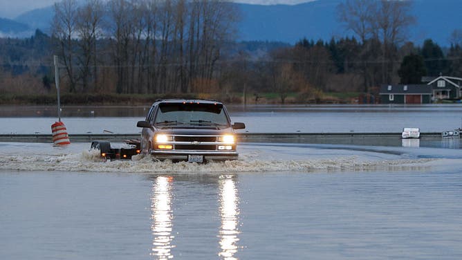 A driver manages to drive through flood waters from the Snohomish River in Snohomish, Washington, on December 11, 2025. Tens of thousands of people were under evacuation orders Thursday in western North America, after days of heavy rain forced rivers to burst their banks. Storms have battered Washington state in the US and British Columbia over the Canadian border for several days, with rivers continuing to rise.