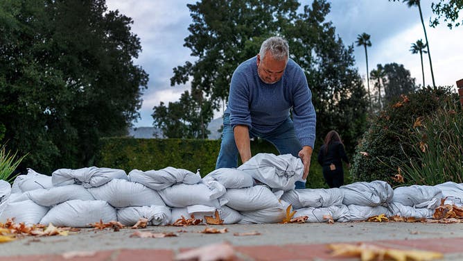 ALTADENA, CA - DECEMBER 23, 2025: Bob Ganguin of Altadena places sandbags at the end of his driveway in preparation for the forecasted storm to arrive Tuesday night on December 23, 2025 in Altadena, California.