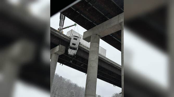 A large semi-truck hangs off the edge of a bridge after crashing in heavy snow conditions.