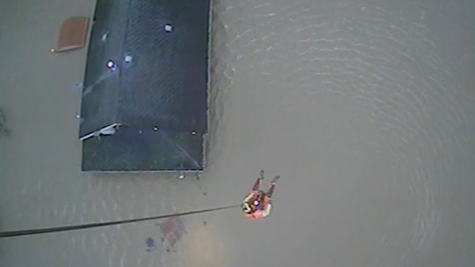 A Coast Guard rescue swimmer rappels down to the roof where the people are trapped in the attic.