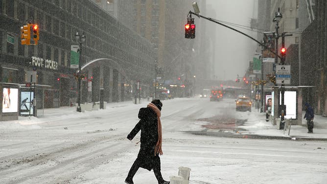 NEW YORK, NEW YORK- JANUARY 25: A passerby crosses the street during a snowstorm on January 25, 2026 in New York City. A low-pressure system is sweeping across the eastern two-thirds of the country, from Texas to New York, dumping up to two feet of snow, coupled with high winds and freezing temperatures, causing flight delays and cancellations in many regions.