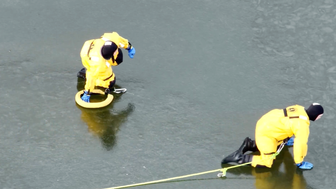 Firefighters carefully crawl across the ice to rescue the stranded deer.