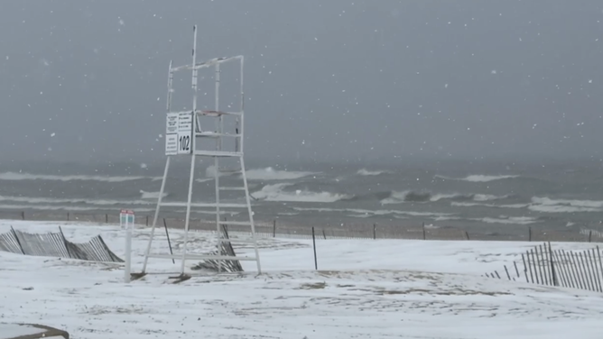 Snow falls on the beach as waves crash in the background along Lake Michigan.