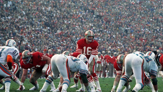 STANFORD, CA - JANUARY 20: Quarterback Joe Montana #16 of the San Francisco 49ers stands behind center Fred Quillan as offensive lineman Randy Cross #51 looks on and as linebacker Mark Brown #51 and defensive linemen Bob Baumhower #73 and Kim Bokamper #58 of the Miami Dolphins are set to pursue the play during Super Bowl XIX at Stanford Stadium on January 20, 1985 in Stanford, California. The 49ers defeated the Dolphins 38-16.