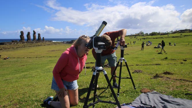 TOPSHOT - A couple prepares their telescopes to view the annular solar eclipse at Easter Island in the Pacific Ocean, Chile, on October 2, 2024.