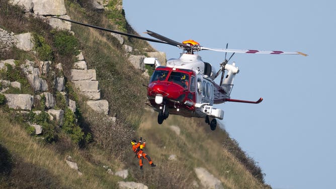 PORTLAND, ENGLAND - OCTOBER 25: HM Coastguard rescue helicopter, (AgustaWestland AW189) raises a winch paramedic during a training exercise on the cliffs, on October 25, 2024 in Portland, United Kingdom.