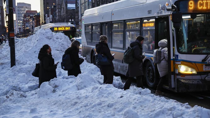 BOSTON, MA - January 29: Commuters board an MBTA bus on January 29, 2026, climbing over snow piled along the curb after storms earlier in the week dumped heavy snowfall across the region.