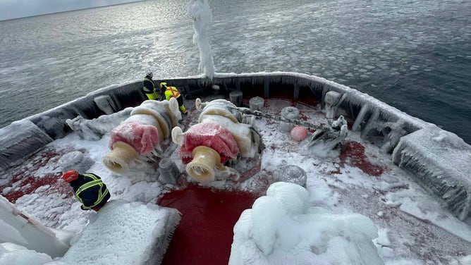Members of the Canadian Coast Guard work to break away large ice accumulations on their boat.