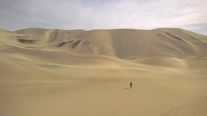 A photo of a person walking across the Eureka Dunes in Death Valley National Park.