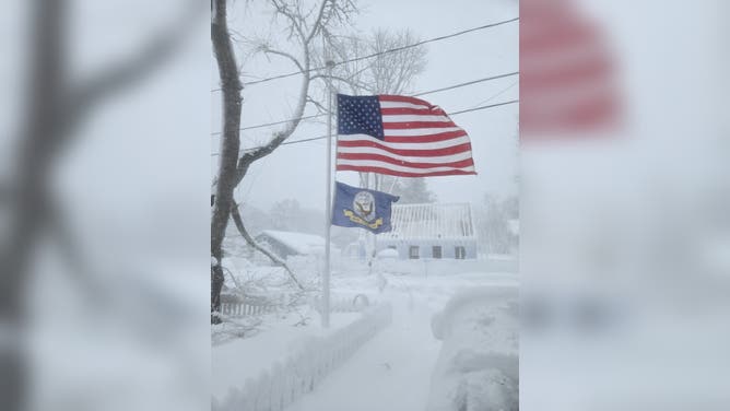 Waving American flag stands amid heavy snowfall in Plymouth, Massachusetts.