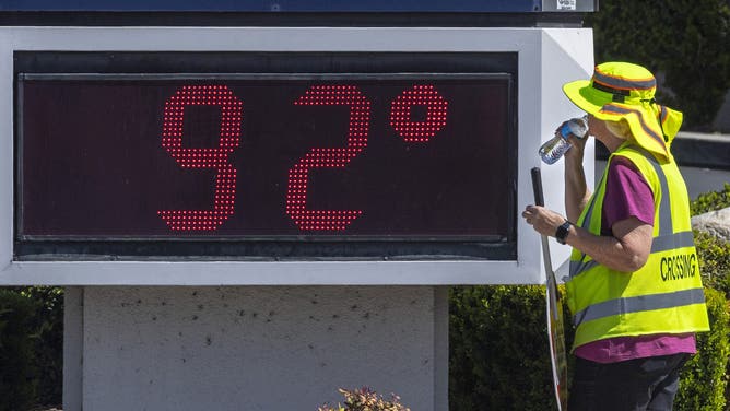 Yorba Linda, CA - April 07: Brenda Verbeck, left, a crossing guard at the intersection of Fairmont and Yorba Linda Boulevards in Yorba Linda, takes a drink as she stands next to a temperature sign that reads 92 degrees on Thursday afternoon, April 7, 2022.