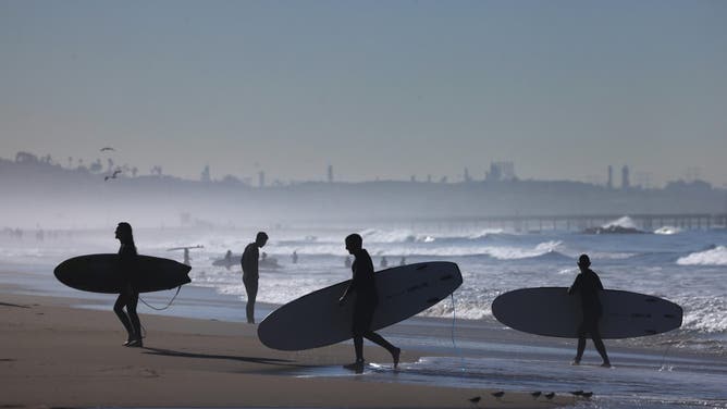 SANTA MONICA, CA - MARCH 13, 2026 Surfers make their way through the early morning mist after catching a few waves in Santa Monica on March 13, 2026.