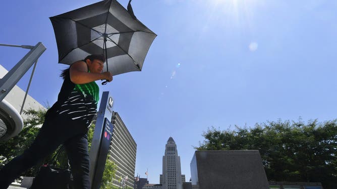 A pedestrian uses an umbrella while walking past City Hall in Los Angeles amid an ongoing heatwave on August 29, 2017