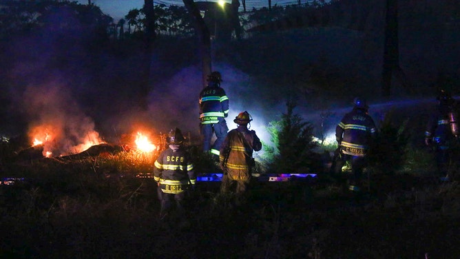 Fire crews work to extinguish a blaze caused by a lightning strike that sent a dinosaur up in flames at Field Station: Dinosaurs in Kansas, April 25.