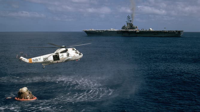 A Navy helicopter flies over the Apollo 17 after it splashes down in the Pacific Ocean. Nearby the aircraft carrier Ticonderoga cruises to pick up the capsule and astronauts. The Apollo 17 was the last flight of humans to the moon.