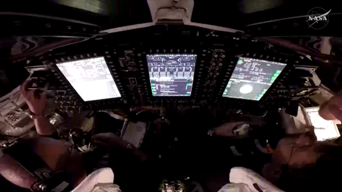 A view over the shoulders of NASA astronauts Victor Glover (left) and Reid Wiseman (right), pilot and commander, respectively, inside the Orion spacecraft as they participate in a proximity operations demonstration.