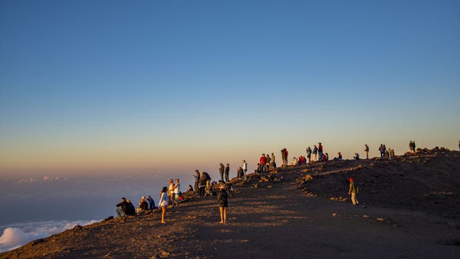Maui, Hawaii, Tourists on the Haleakala Crater in the Haleakala National Park watch the sunset while above the clouds.