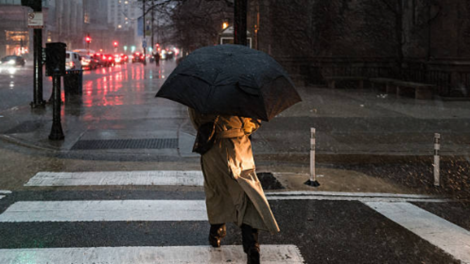A woman walks with difficulty in the heavy rain as a winter storm brings snow and gusty winds, creating challenging travel conditions on roads and at airports in Chicago, United States, on March 15, 2026. Nearly 500 flights at Chicago's O'Hare Airport are canceled and hundreds more delayed as the storm disrupts travel nationwide.