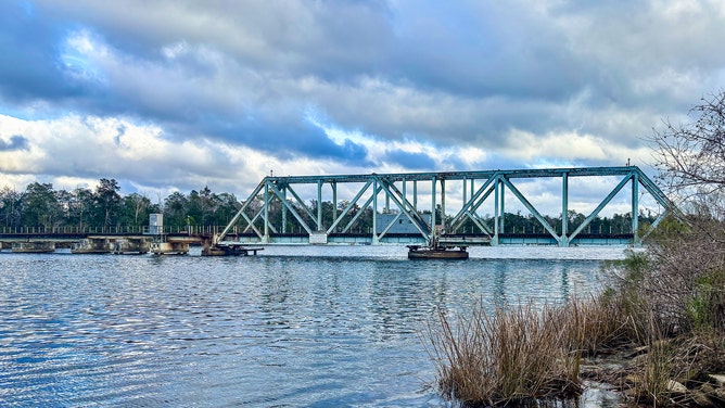 A scenic view of the Blackwater River Swing Bridge spanning the Blackwater River in Milton, Florida, on a partly cloudy day.
