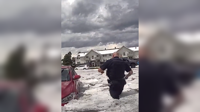 Aurora Police officer trudges through hail-covered floodwaters to rescue stranded woman.