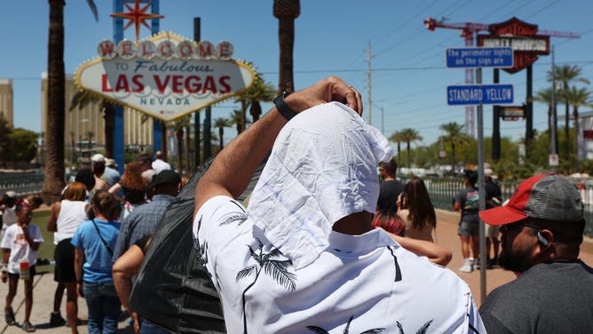 A man shields himself from the sun while waiting in line to take a photo at the historic Welcome to Las Vegas Sign during a heat wave in Las Vegas, Nevada, on July 14, 2023.