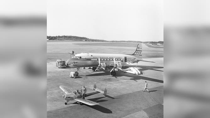 1950s airport. A Douglas DC-4 of Pan American World Airways "Clipper Oslo" PA-A N88944 being prepared and fueld before takeoff. A man is seen on the wing at the end of the gas pipe from the truck. The smaller propeller aircraft is a Ercoupe 415 SE-BNA with a man with a briefcase about to step into the aircraft. Sweden 1953. Kristoffersson ref BM42-3