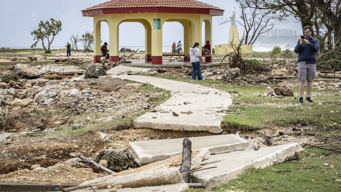 A man takes photographs of a damaged walkway at a park in the aftermath of Super Typhoon Bavi in Guam on July 7, 2026.