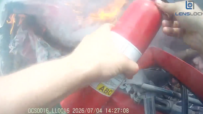The deputy uses another fire extinguisher to spray the large flames on the car.