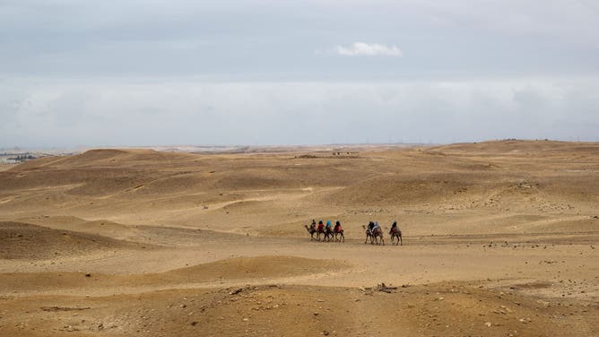 Tourists ride camels in the desert outside the Giza pyramids necropolis on the southwestern outskirts of the Egyptian capital on March 13, 2020.