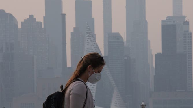 WEEHAWKEN, NJ - JUNE 7: A woman wears a face mask as smoke continues to shroud the sun as it rises behind the skyline of Manhattan in New York City on June 7, 2023, as seen from Weehawken, New Jersey.