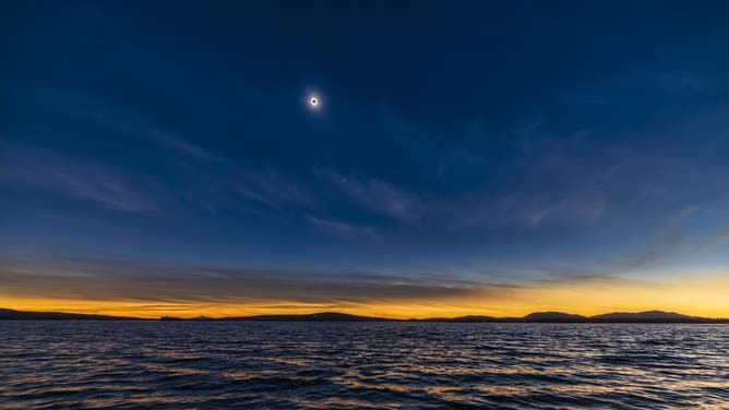 This is the total eclipse of the Sun over the waters of Lac Brome, in the Eastern Townships of Quebec, Canada, on April 8, 2024. The twilight sky colours are from the light of the Sun from areas outside the path of totality. This is looking southwest, the direction toward the eclipsed Sun but (to the right) also the direction the lunar shadow arrived from and where the sky brightened first at the end of totality. This is from the Tiffany Park area of Lac Brome in the Eastern Townships of Quebec, on the east side of the lake where several dozen cars and eclipse chasers gathered this day for a fine view. The bright object below the eclipsed Sun is Venus. High cirrus clouds added to the sky colouration and visibility of the shadow passage. This was taken near mid-eclipse. This is a single 1/6s-exposure from a 1200-frame time-lapse, with the Canon RF15-35mm lens at f/2.8 and Canon Ra at ISO 125. Sky detail and contrast emphasized with Luminar Neo Enhance filters.